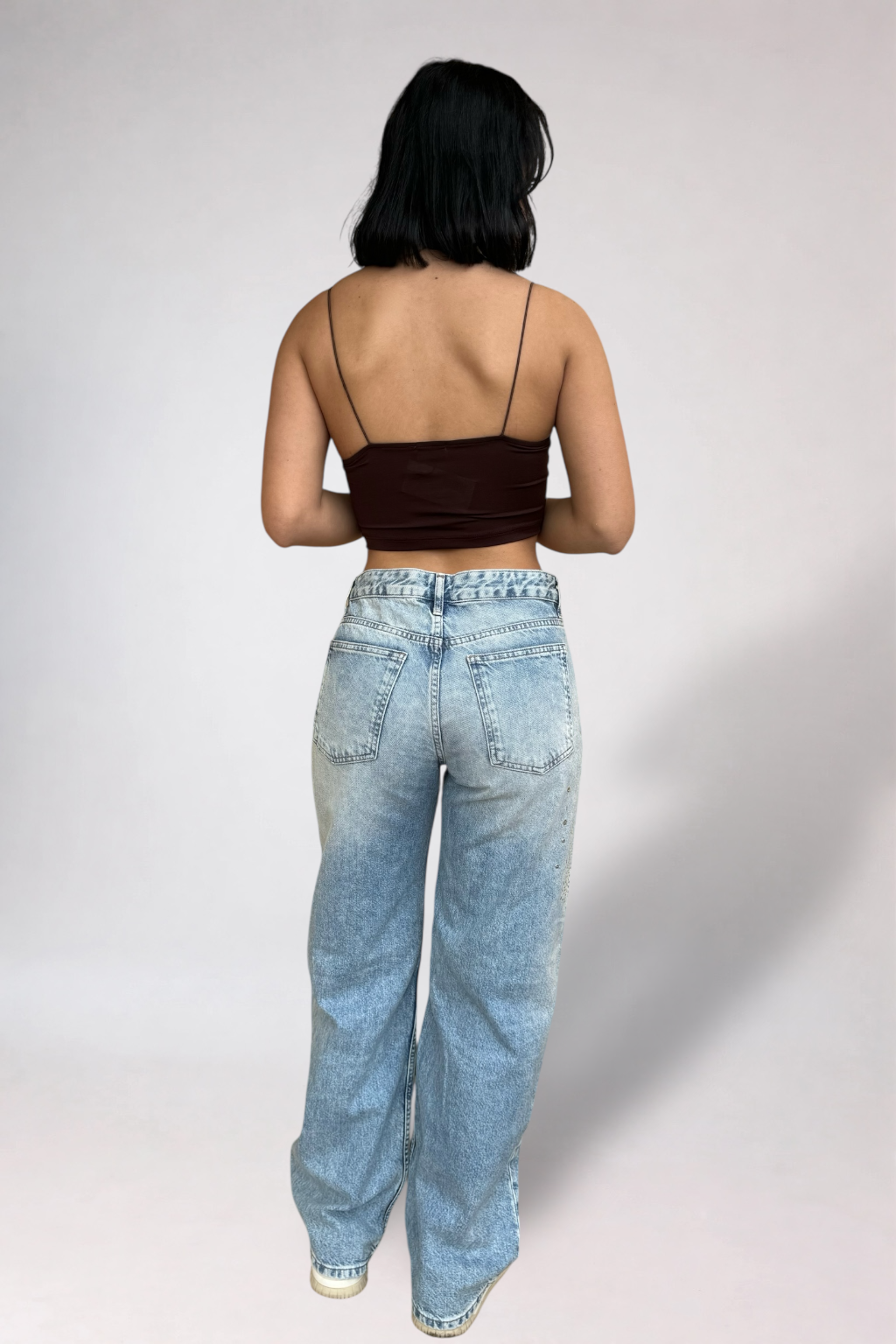 Person wearing a brown top and light blue jeans on a plain background