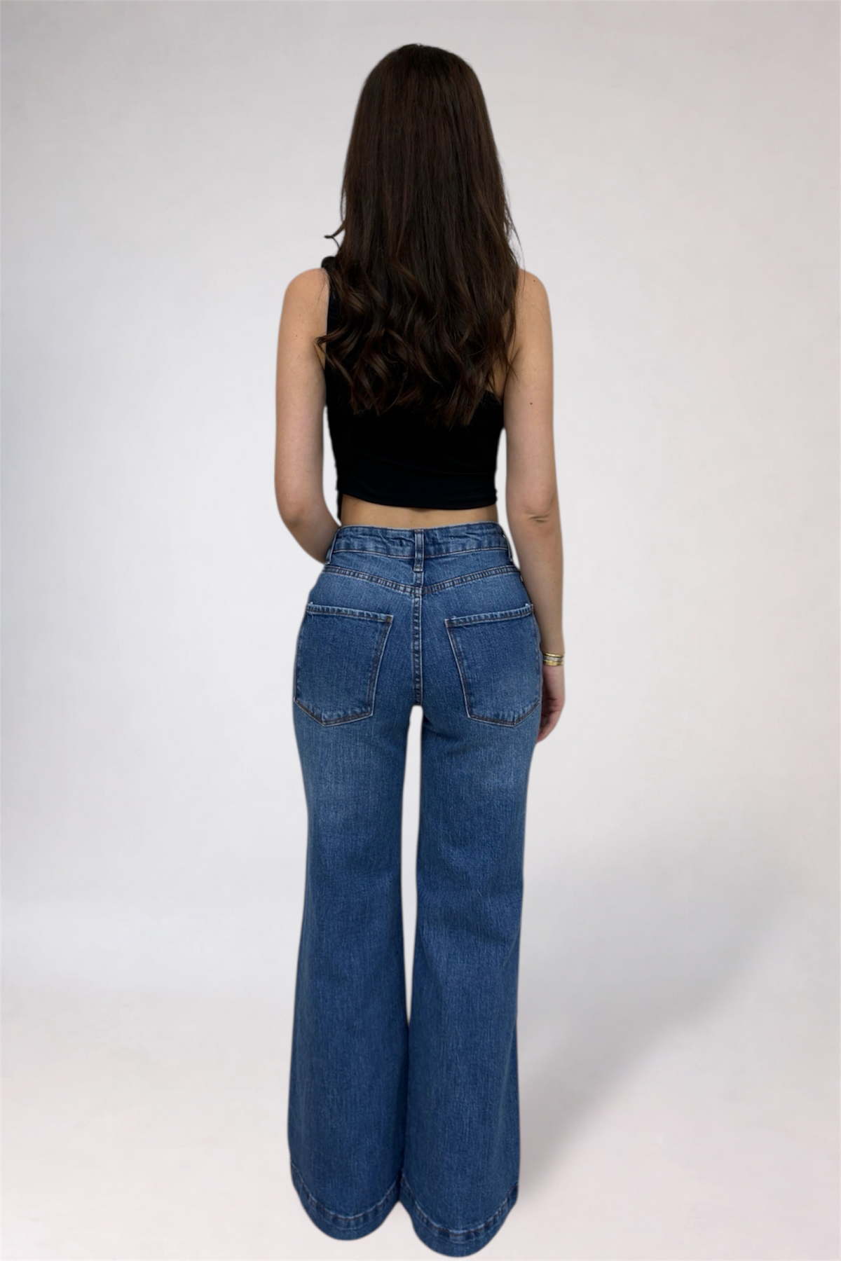 Person wearing blue jeans and a black top on a white background