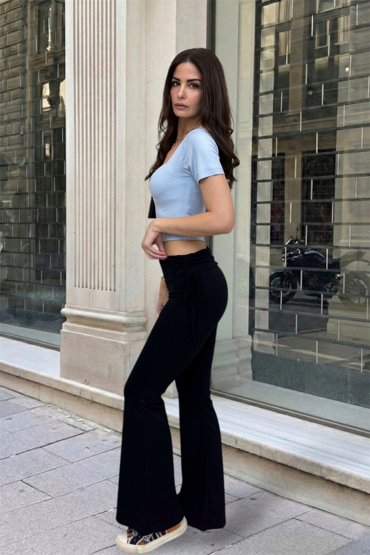 Woman wearing a light blue top and black high-waisted pants standing in front of a building.