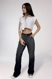 Woman wearing a white sleeveless top and dark jeans on a plain background