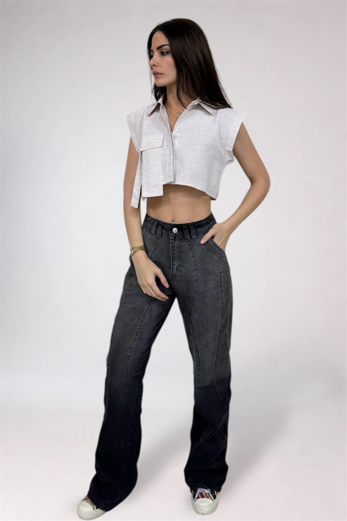 Woman wearing a white sleeveless top and dark jeans on a plain background