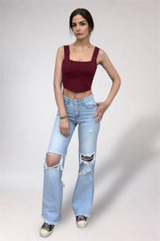 Woman wearing a burgundy top and light blue ripped jeans on a plain background
