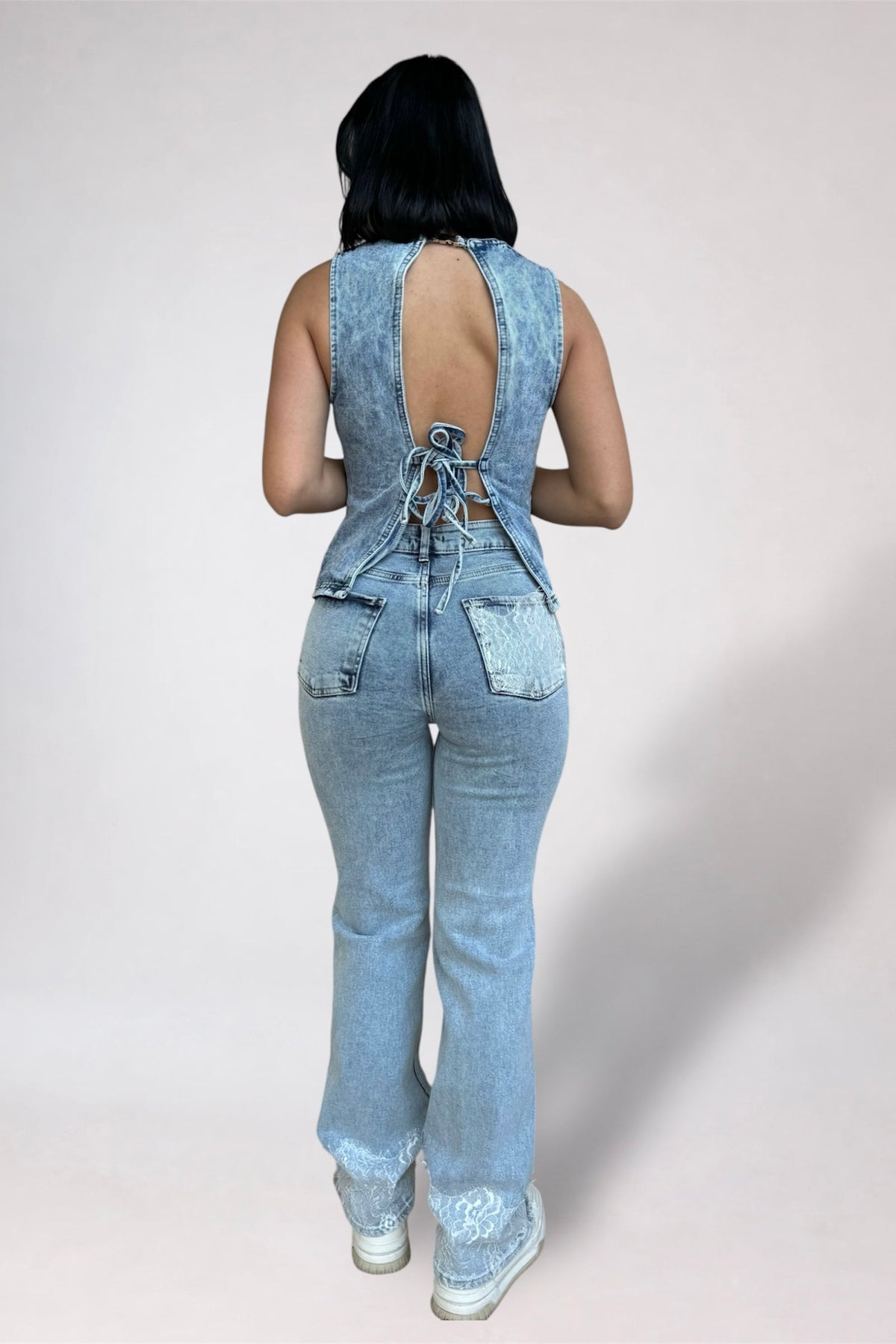 Person wearing a denim jumpsuit with open back on a plain background