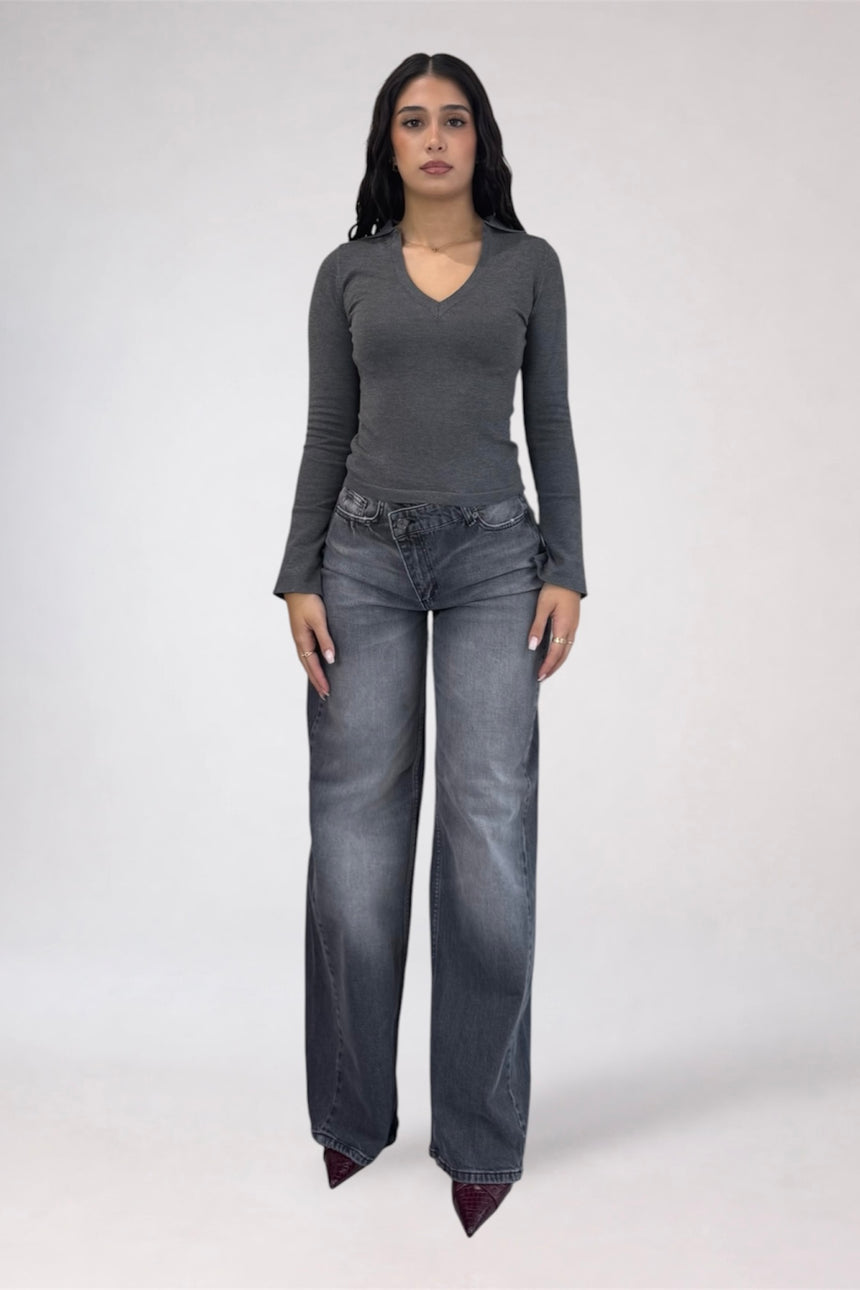 A woman modeling a dark gray long-sleeve V-neck top and wide-leg gray jeans against a plain light gray studio background.