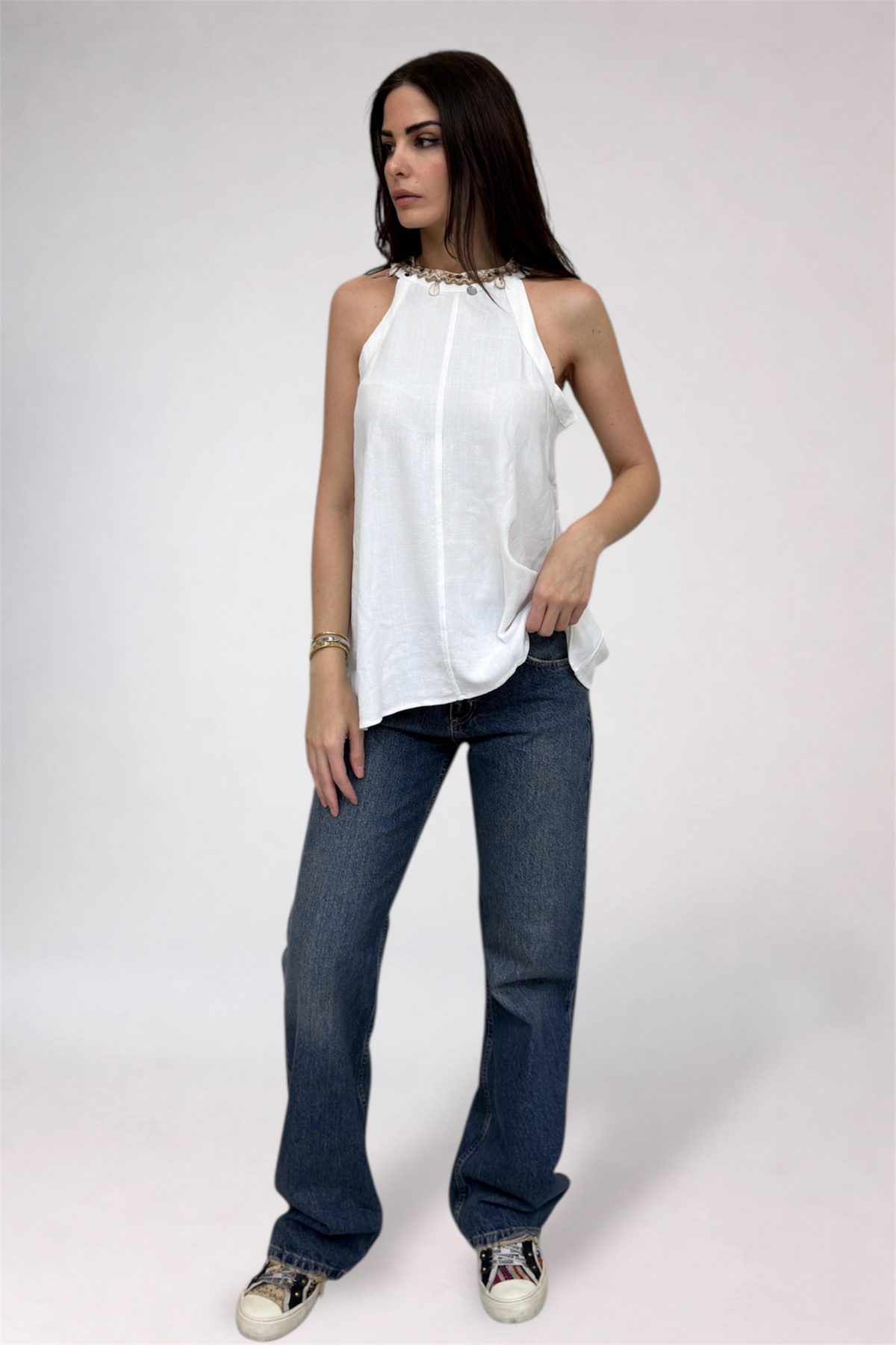 Woman wearing a white sleeveless top and blue jeans on a white background