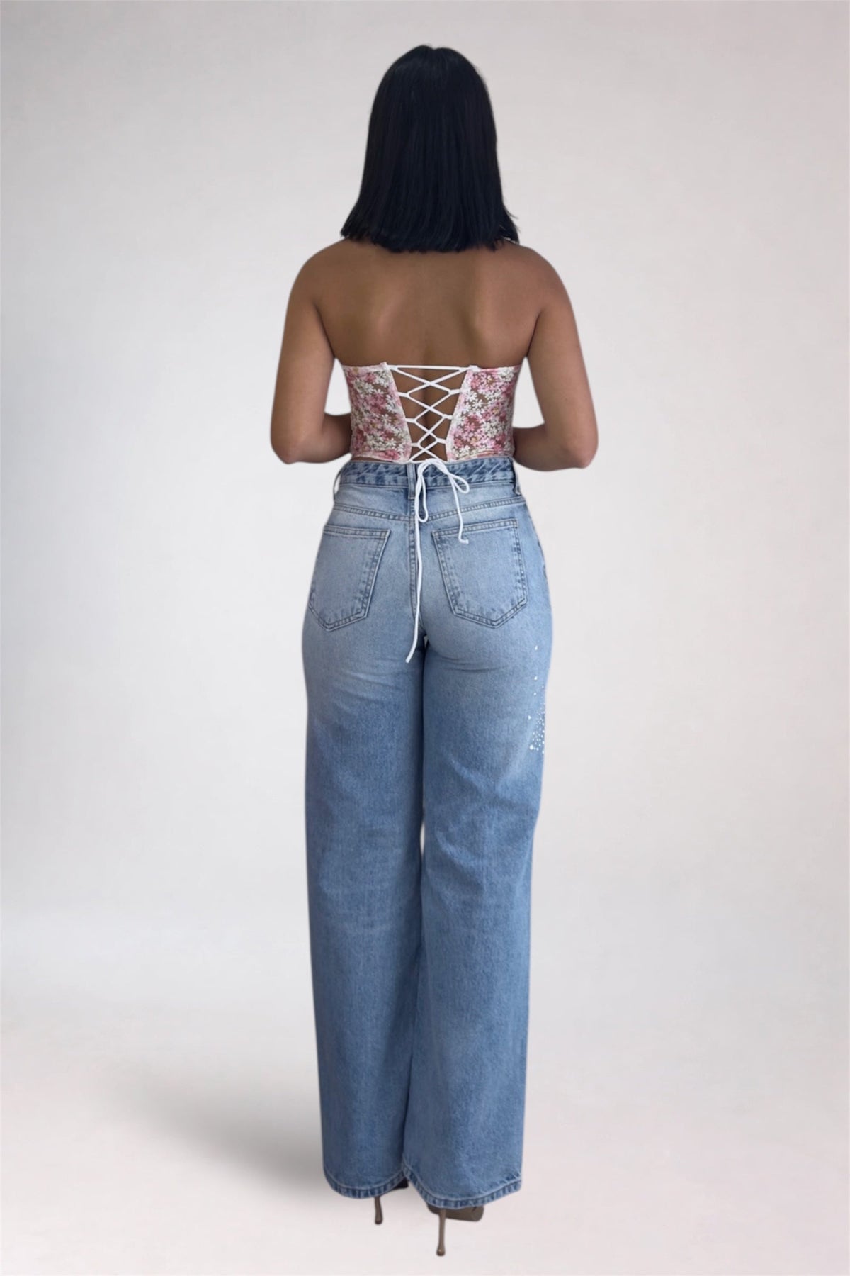 Person wearing a strapless floral top and high-waisted jeans on a plain background