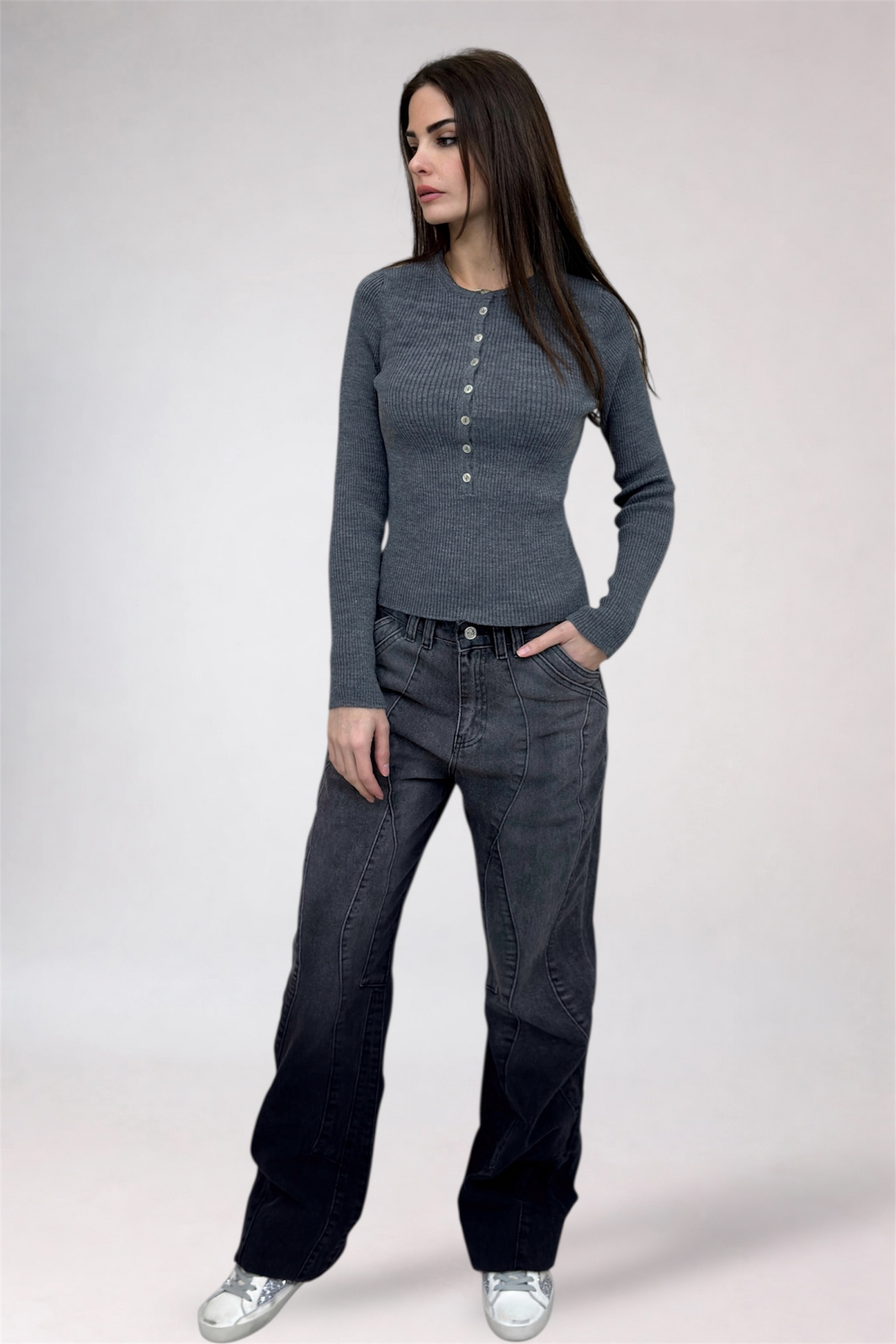 Woman wearing a gray long-sleeve top and dark jeans on a white background