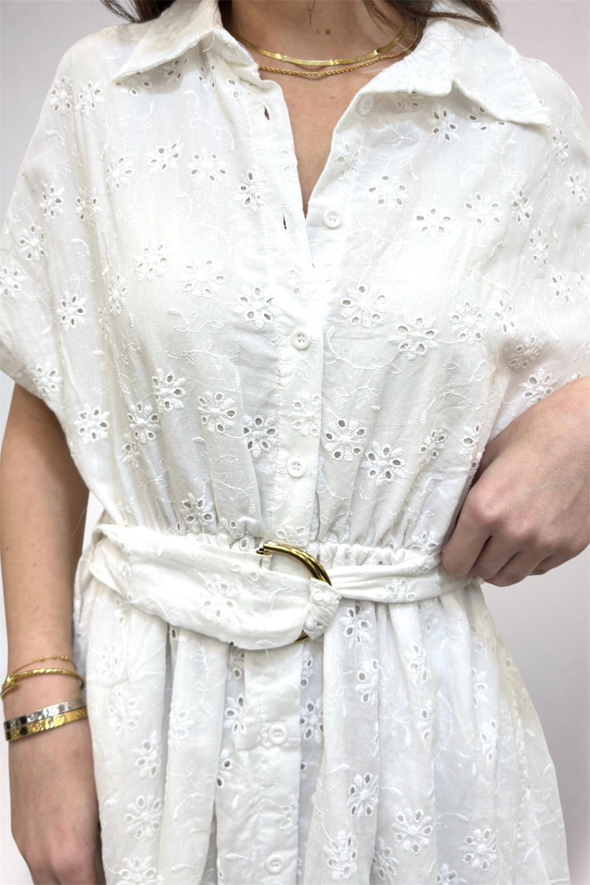White dress with floral patterns worn by a person on a plain background
