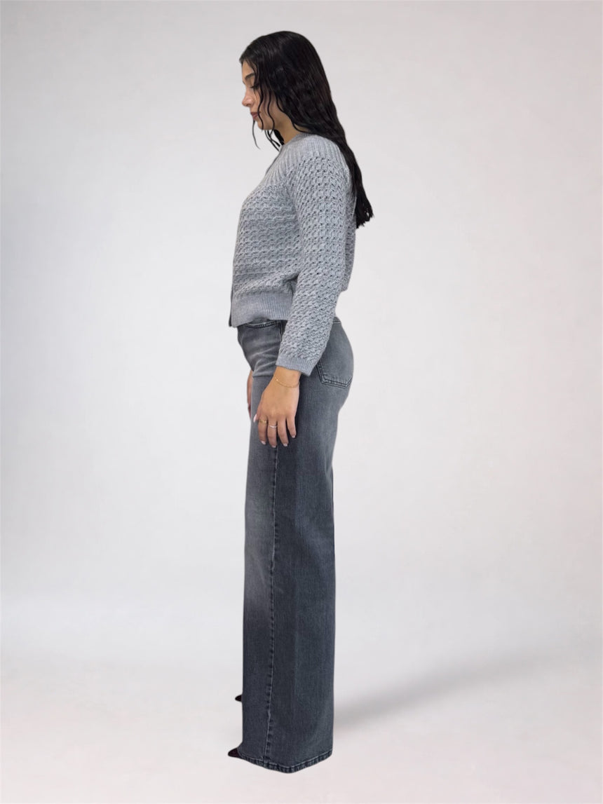 A woman shown in profile wearing a light gray textured knit sweater and dark gray wide-leg jeans against a plain light gray studio background.