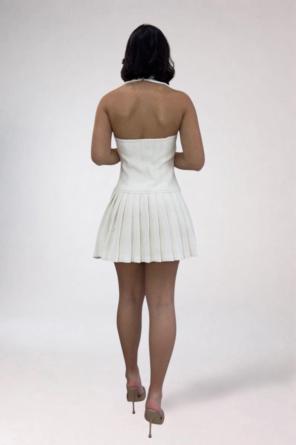 Person wearing a white pleated dress on a plain background