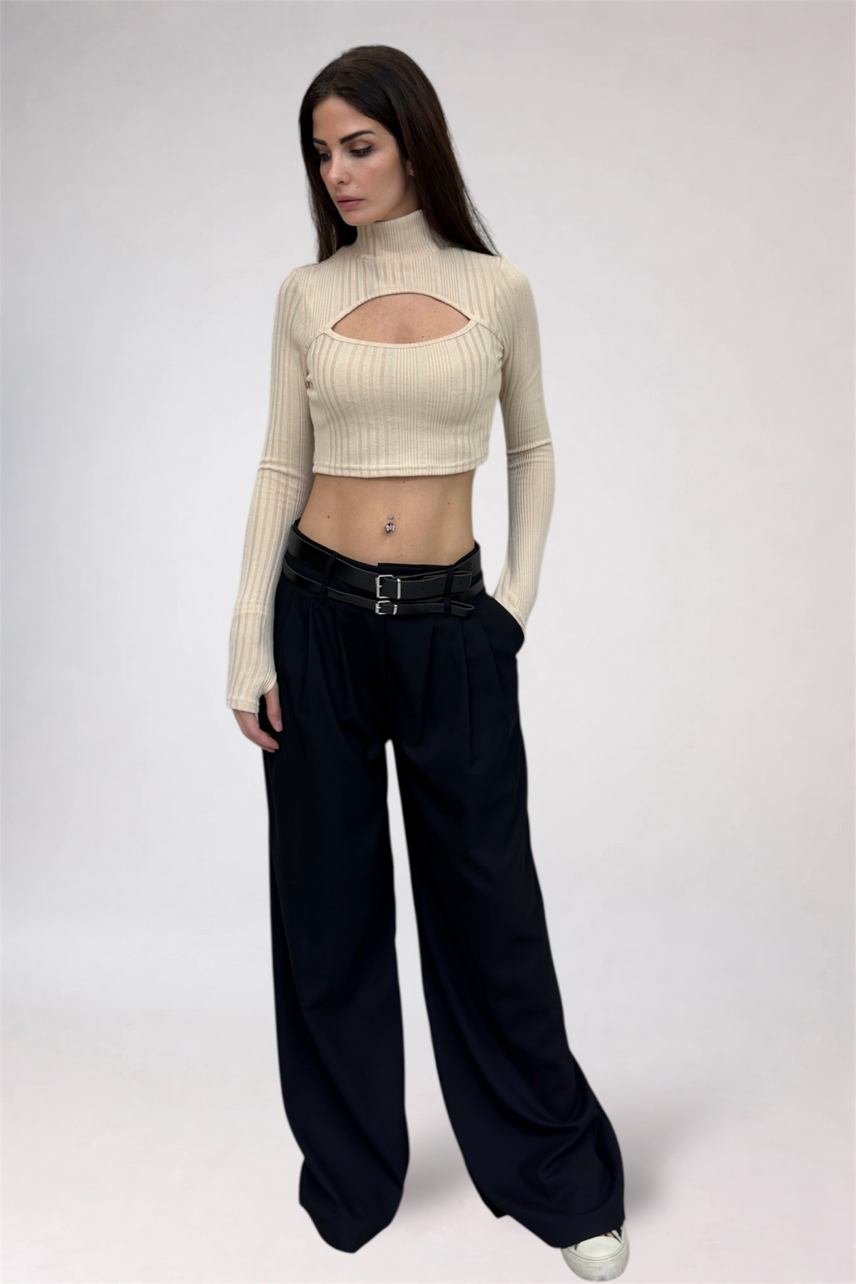Woman wearing a beige cut-out top and black wide-leg pants on a white background