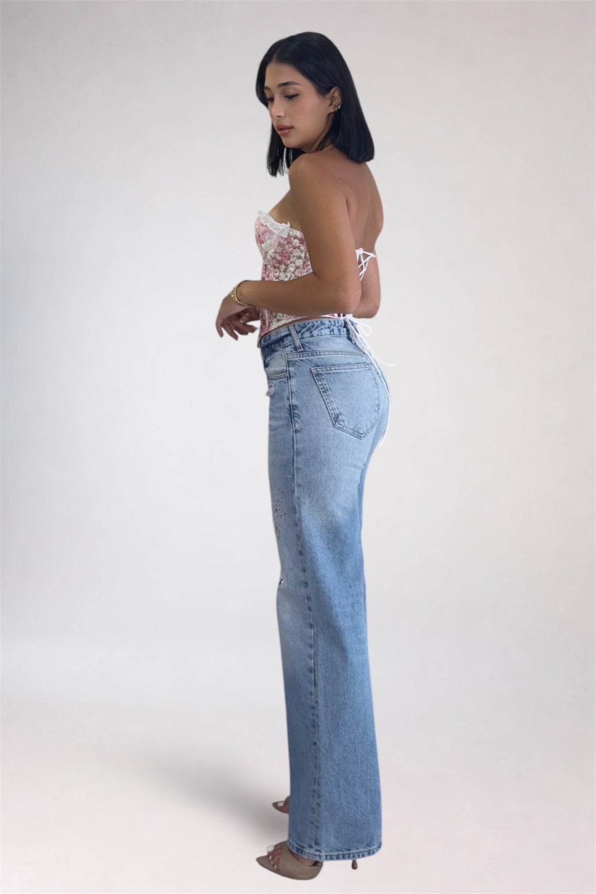 Woman wearing light blue jeans and a floral top on a white background