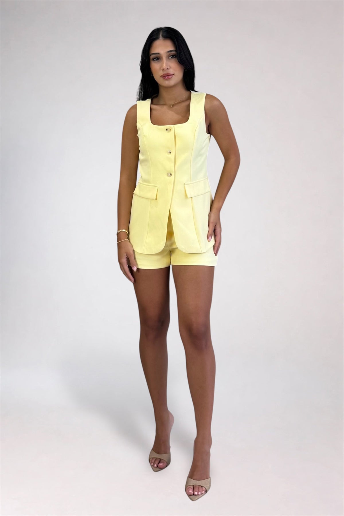 A woman modeling a light yellow sleeveless vest and matching shorts set against a plain light gray studio background.