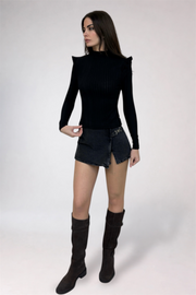 Woman wearing a black long-sleeve top and denim skirt with knee-high black boots on a white background