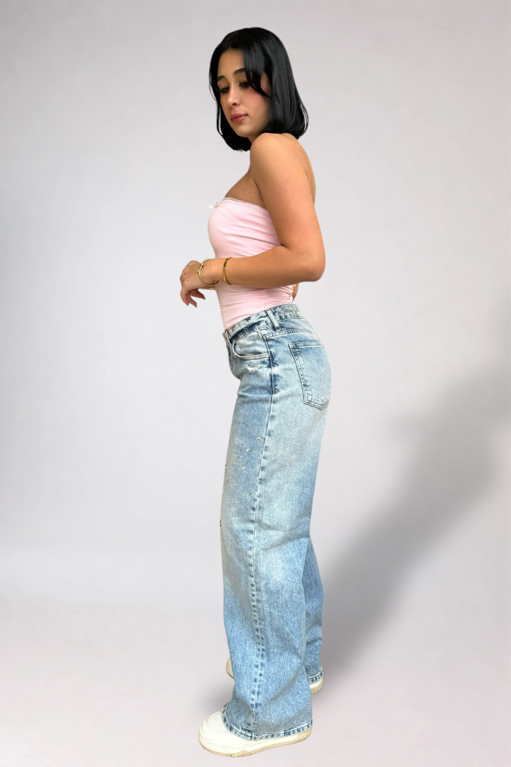 Woman wearing a light pink top and blue jeans against a plain background
