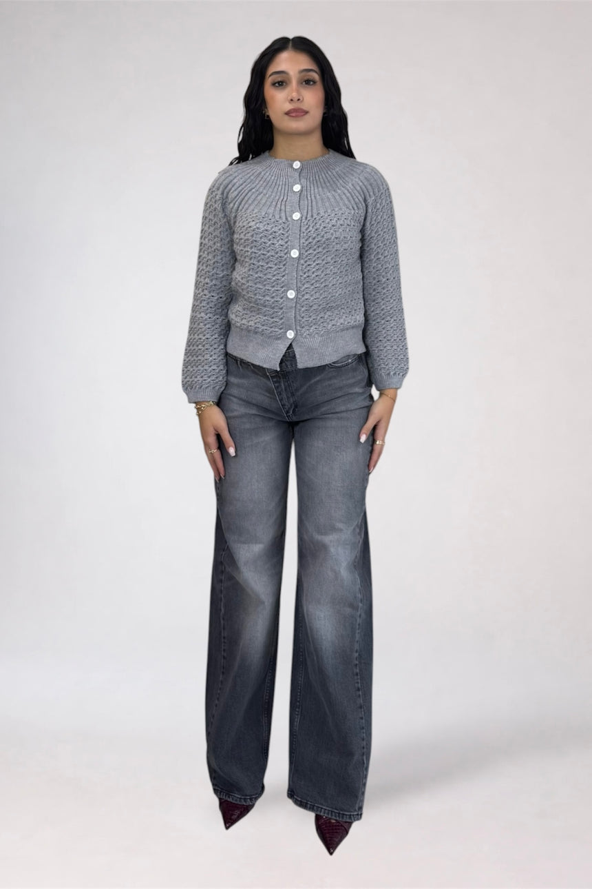 A woman modeling a gray textured knit cardigan with white buttons and dark gray wide-leg jeans against a plain light gray studio background.