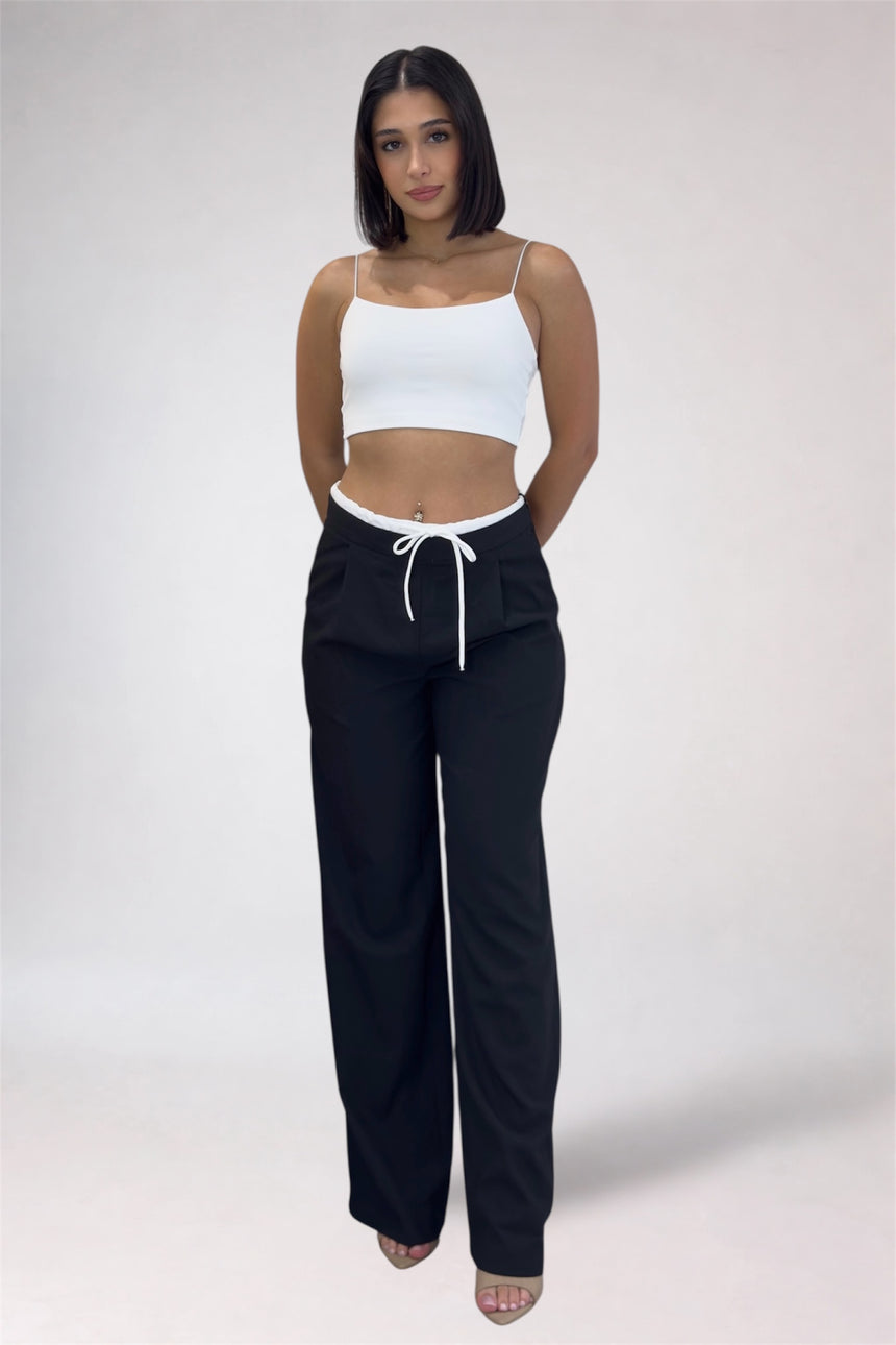 Woman wearing a white crop top and black pants with a drawstring on a plain background