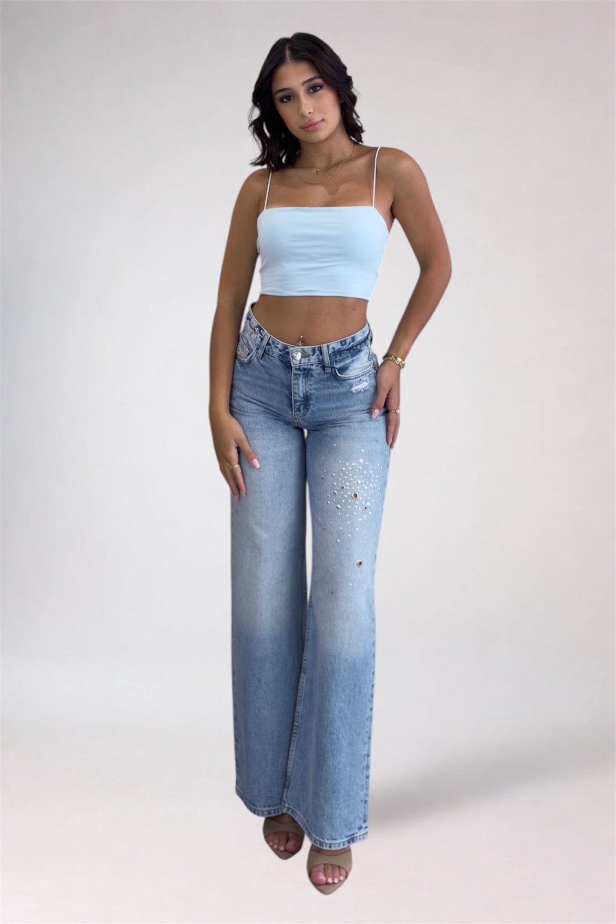 Woman wearing a light blue crop top and high-waisted jeans on a white background
