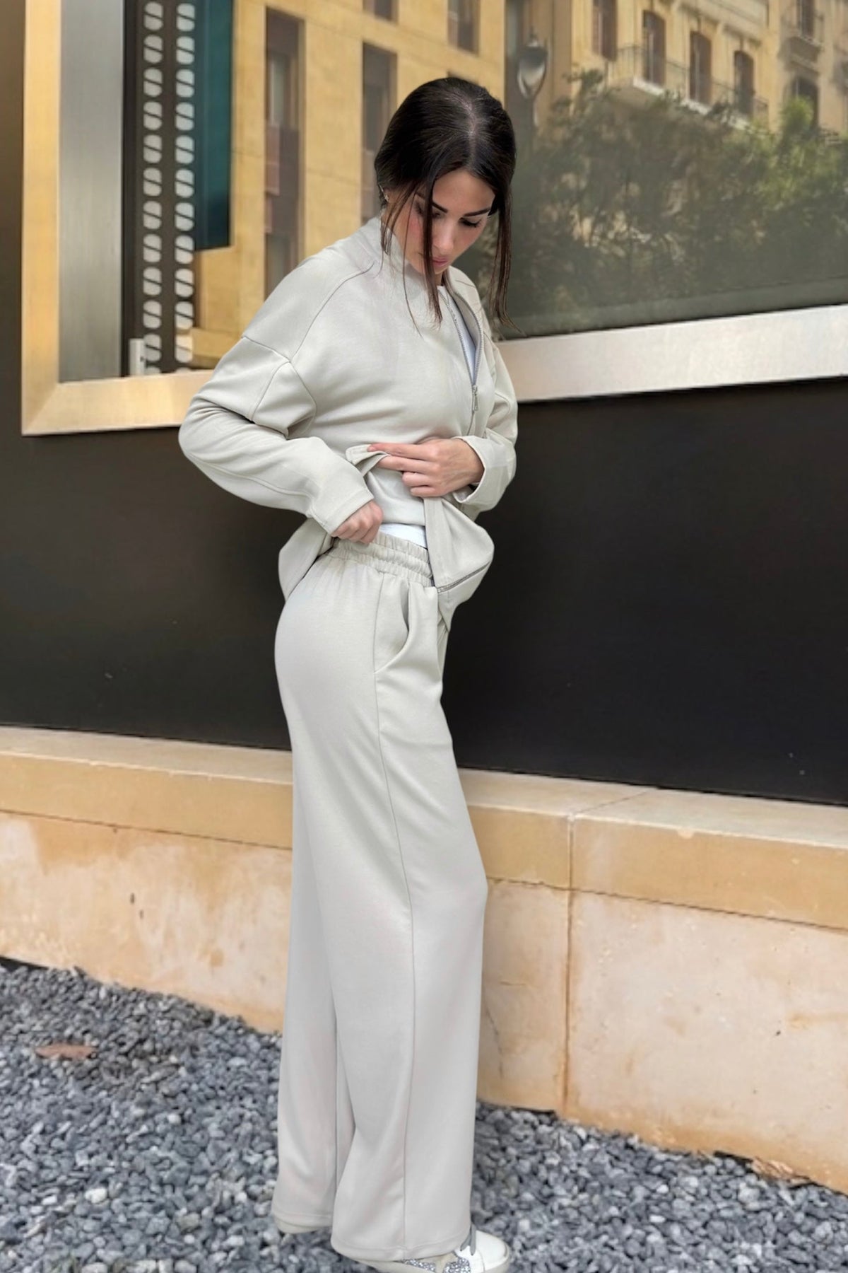 Woman wearing a beige suit standing against a light beige wall.