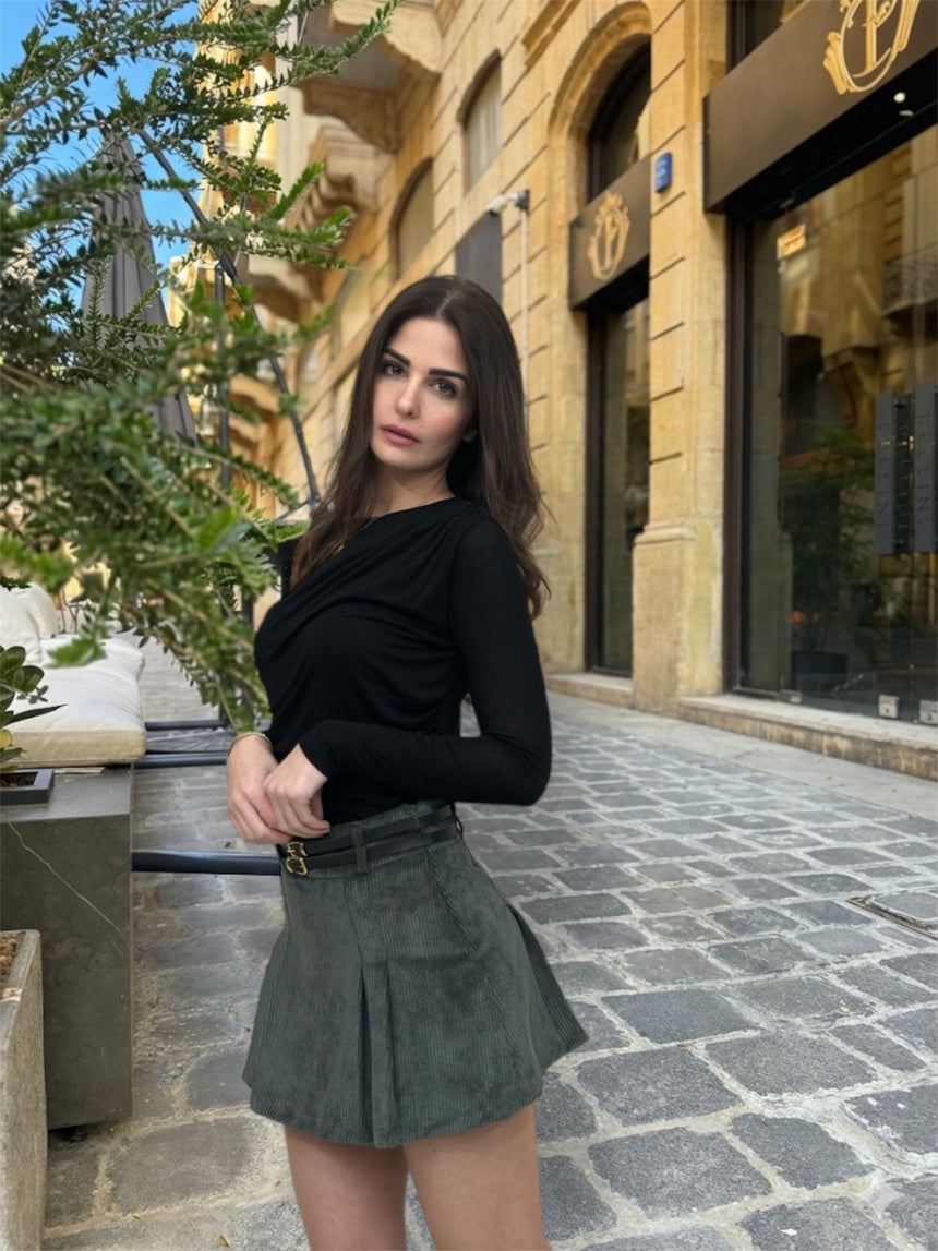 Woman in black top and green skirt standing on a street with buildings in the background