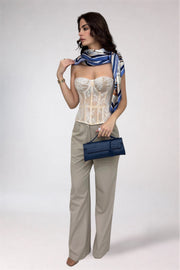 Woman wearing a white lace top and beige pants with a blue scarf and clutch on a white background