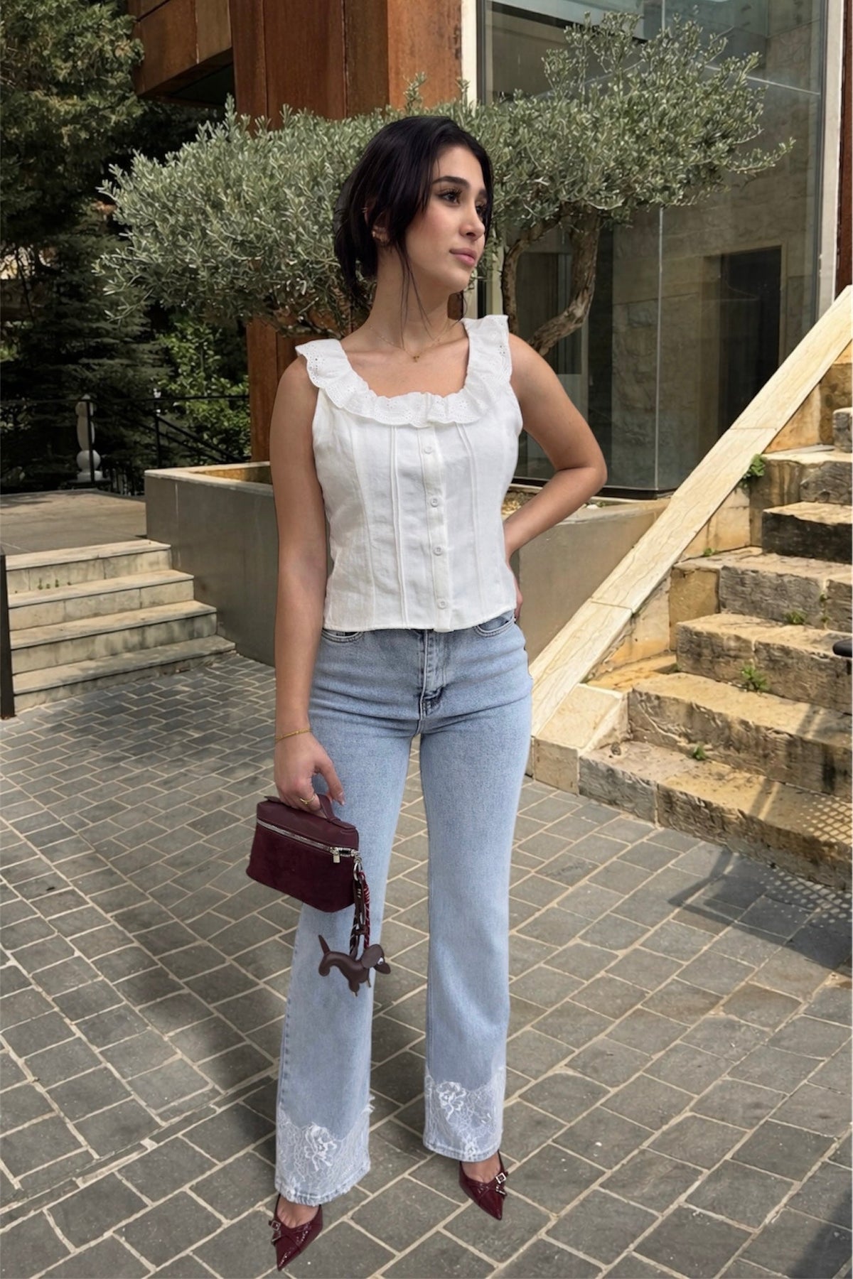 Woman in a white top and light blue jeans standing outdoors on a stone pavement.