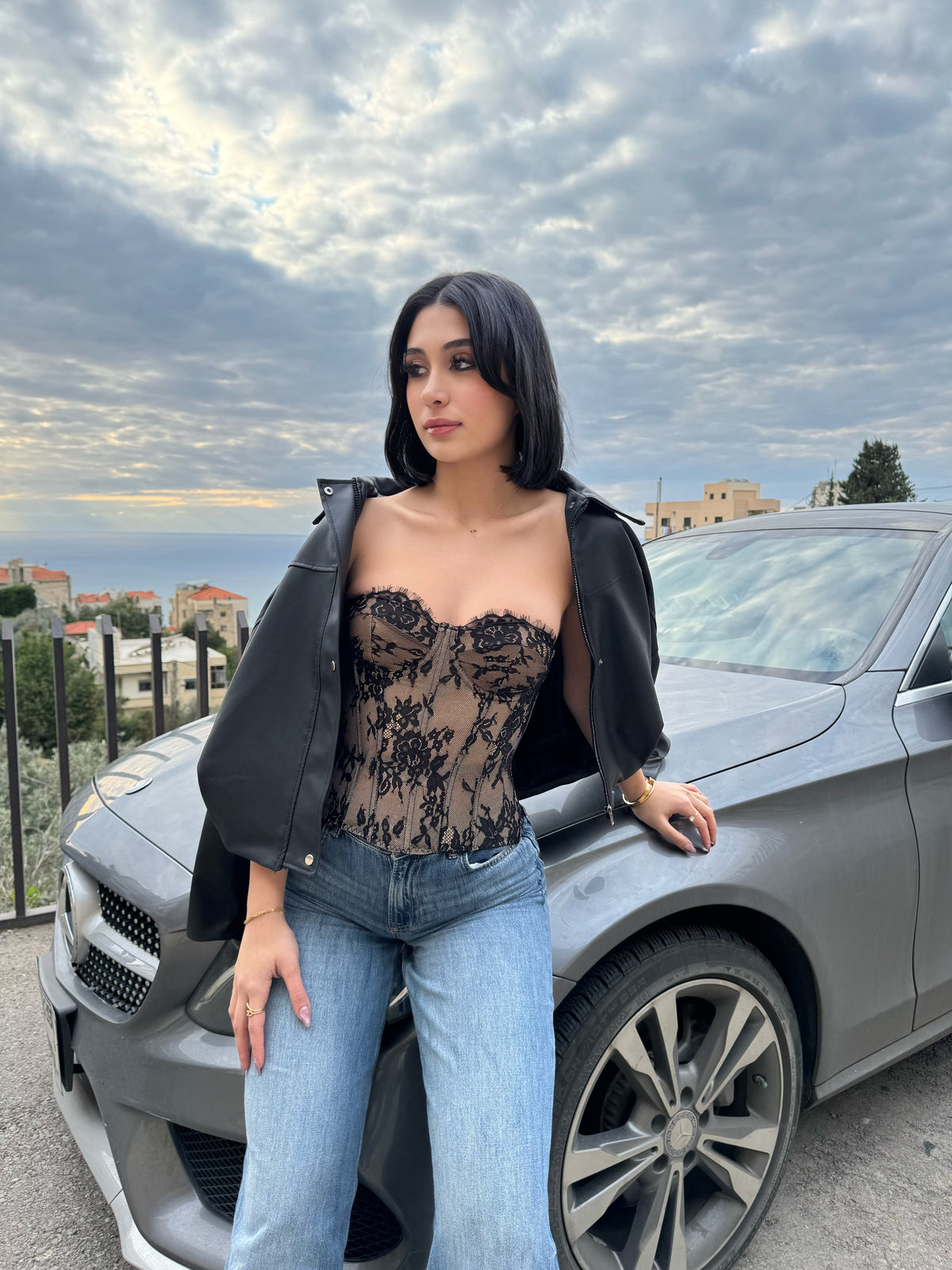 Woman in a lace top and jeans standing next to a car with a scenic background
