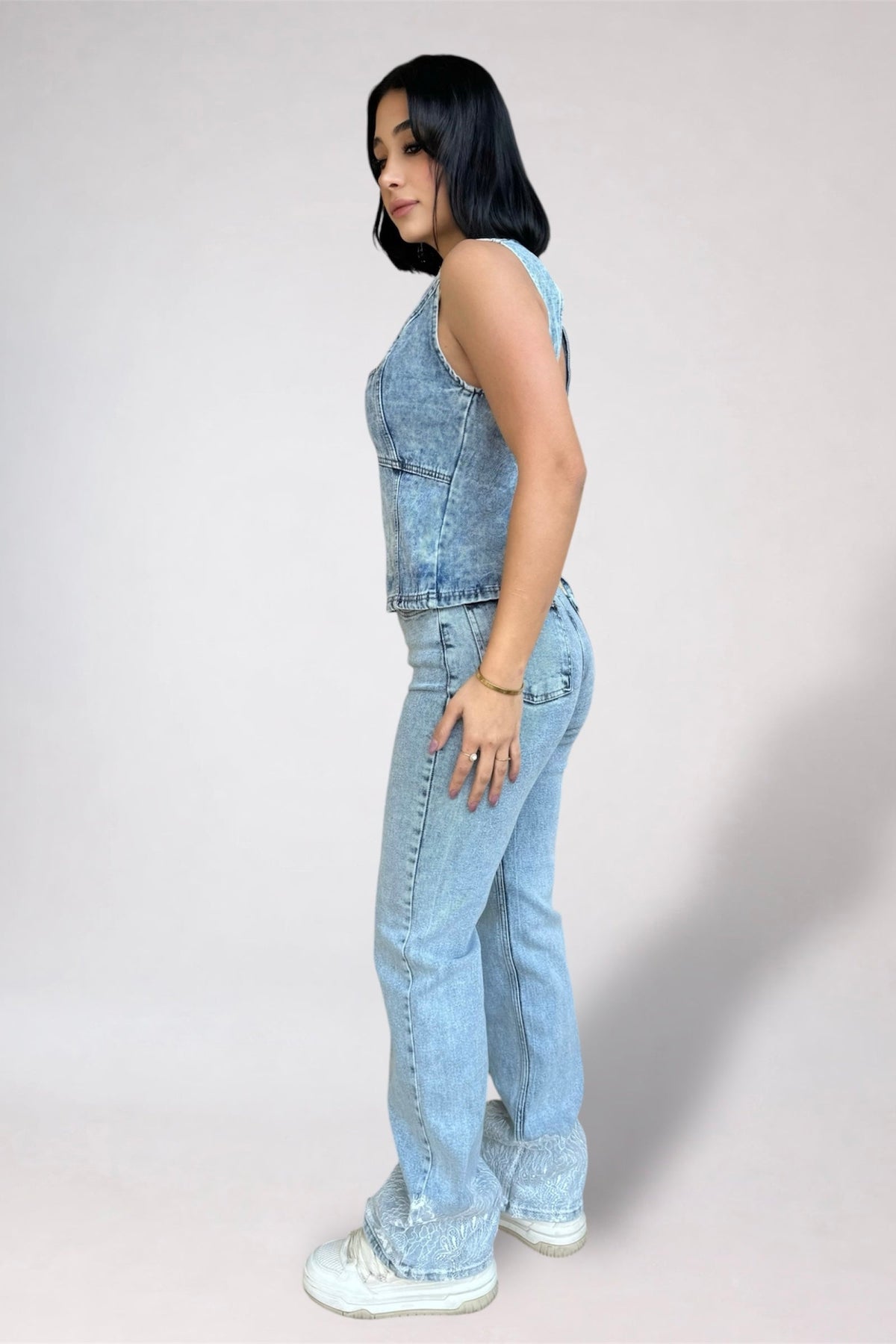 Person wearing a denim sleeveless top and jeans on a plain background