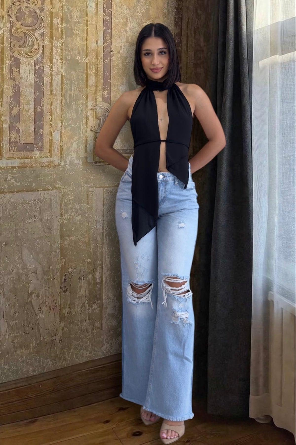 Woman wearing a black top and light blue jeans with a scarf in an indoor setting.