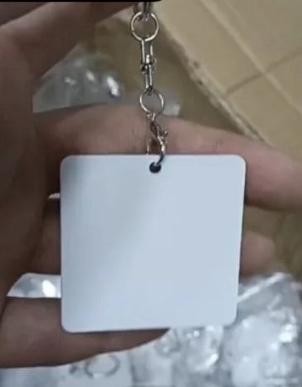 A blank white square metal keychain tag with a silver metal split ring and clasp, held by a hand.