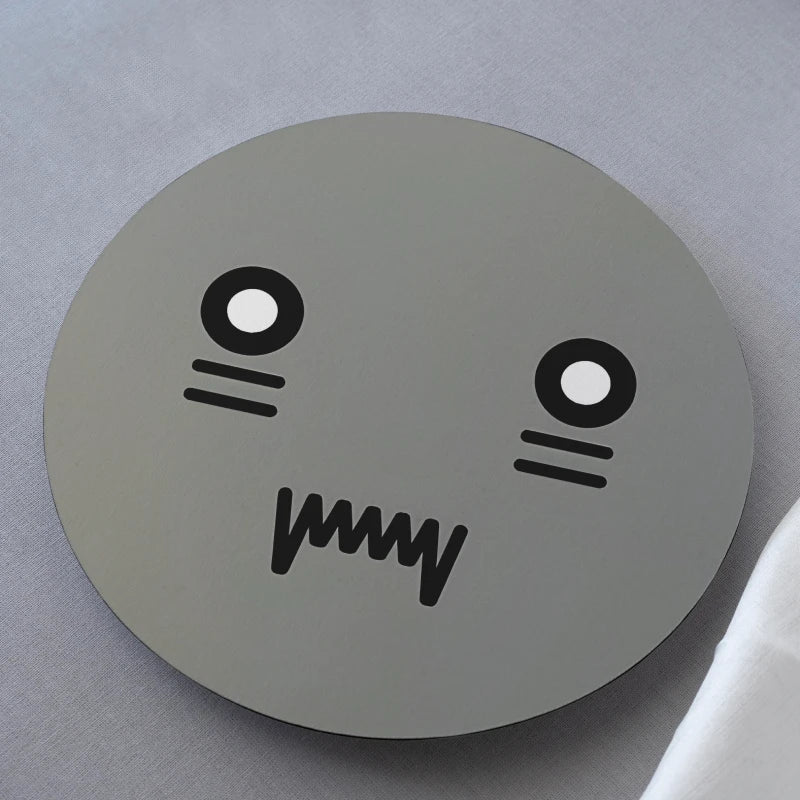 Round gray coaster with a cartoon face design on a light gray background
