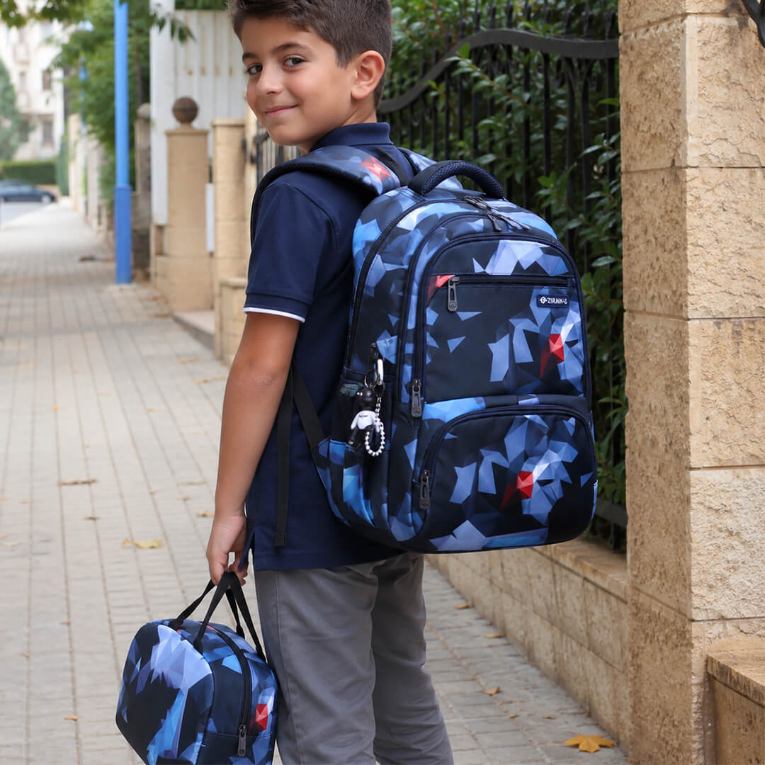 A boy wearing a geometric navy blue school backpack and matching lunch bag 