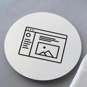 A round, white coaster with a customized black image of a web page design, placed on a soft surface.