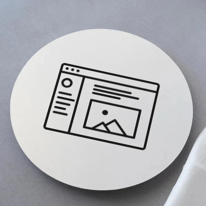A round, white coaster with a customized black image of a web page design, placed on a soft surface.