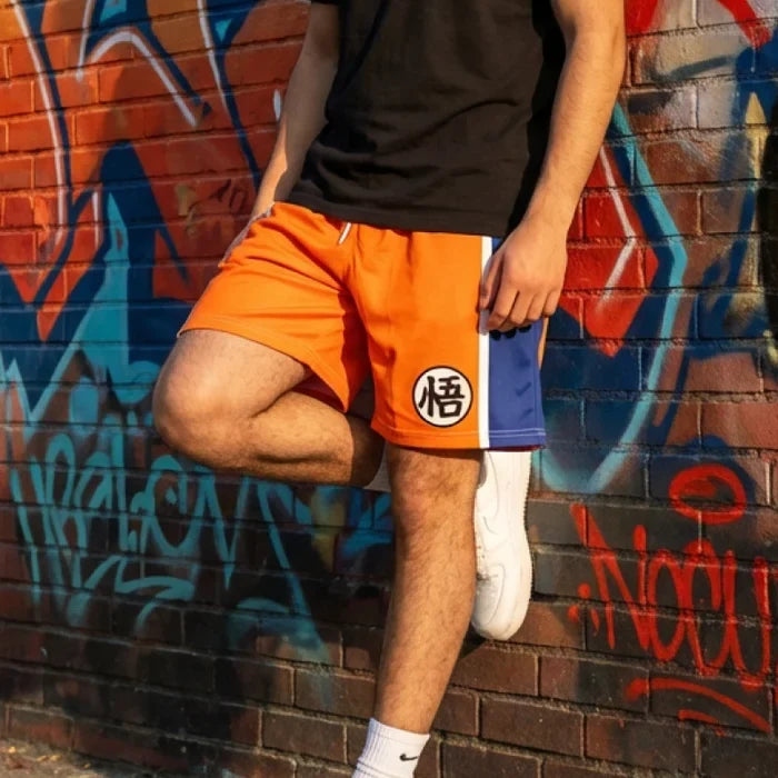 Person wearing orange shorts with a logo, white sneakers, and black shirt against a graffiti-covered wall.
