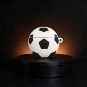 A soccer ball-shaped white and black case for apple airpods displayed on a round black pedestal against a dark background with warm lighting.