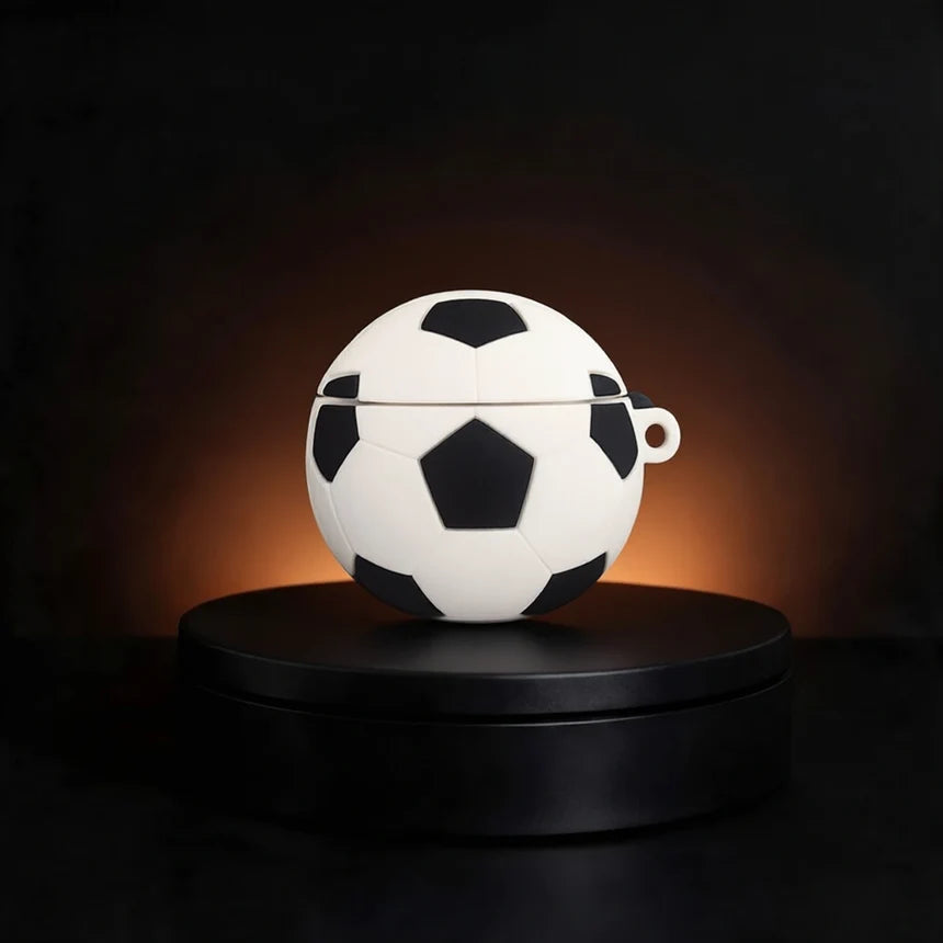 A soccer ball-shaped white and black case for apple airpods displayed on a round black pedestal against a dark background with warm lighting.
