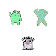 Three frog-themed enamel pins on a plain white background: a light green frog raising one paw, a mint green flexing frog outlined in gold, and a white and gray frog with pink cheeks and the text 'MY FLABBERS ARE GASTED' in black.