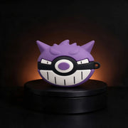 A purple Gengar-themed wireless earbud charging case cover displayed on a black circular pedestal against a dark background with warm lighting.