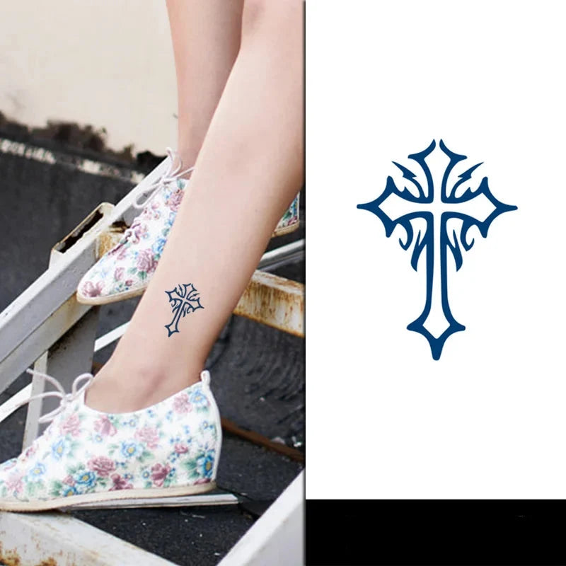 Tattoo of a blue cross on a person's ankle with floral shoes and a white background.