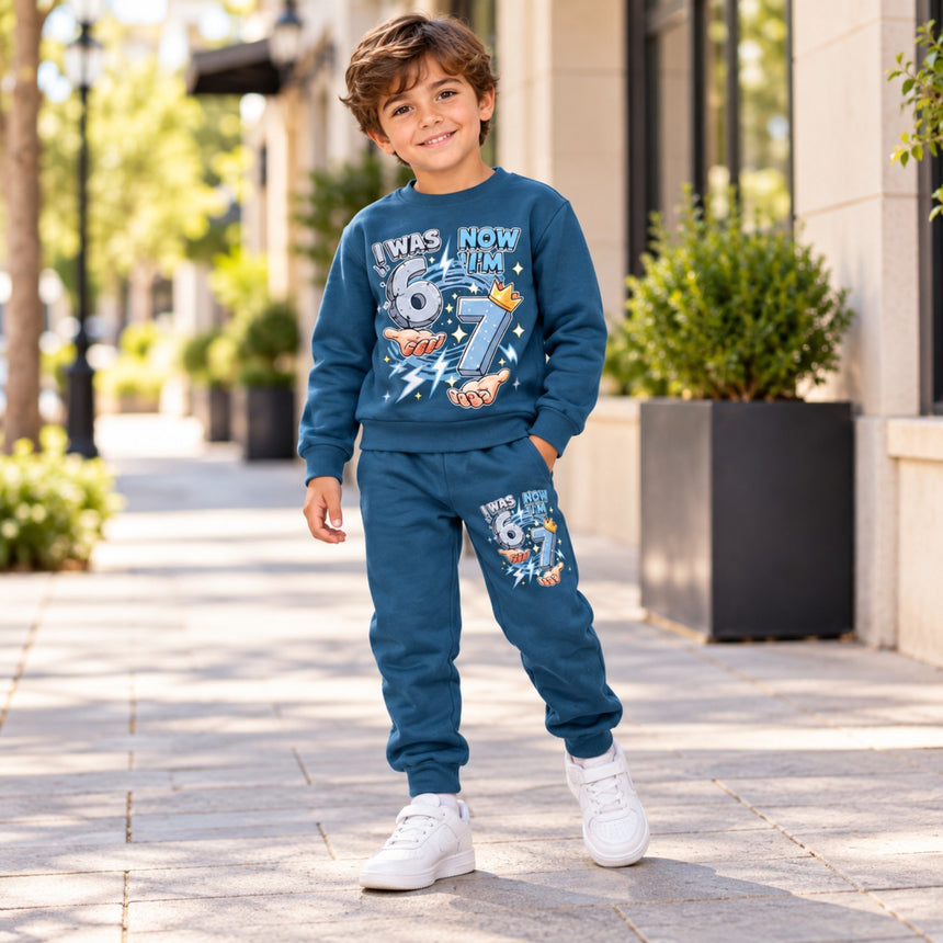 Boys blue two-piece sweatshirt and joggers set with 7th birthday graphic, standing outdoors