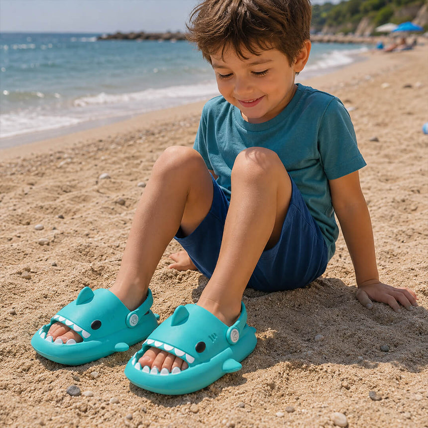 Child wearing teal shark sandals on a sandy beach 