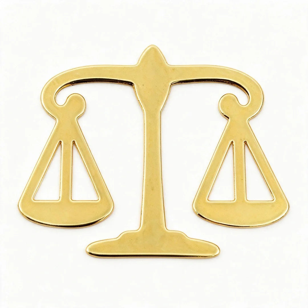 A polished gold-colored metal scale of justice pendant or emblem, shown against a plain white background.