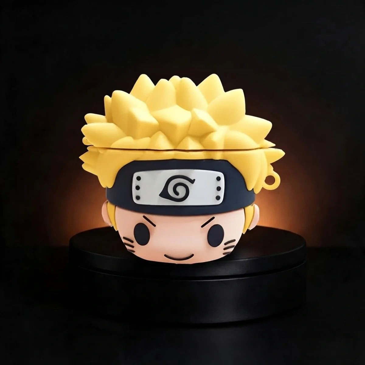 A Naruto-themed AirPods case shaped like the character's face, with spiky blond hair, a black headband, and a small LED light glowing from within, displayed on a black circular base against a dark background.