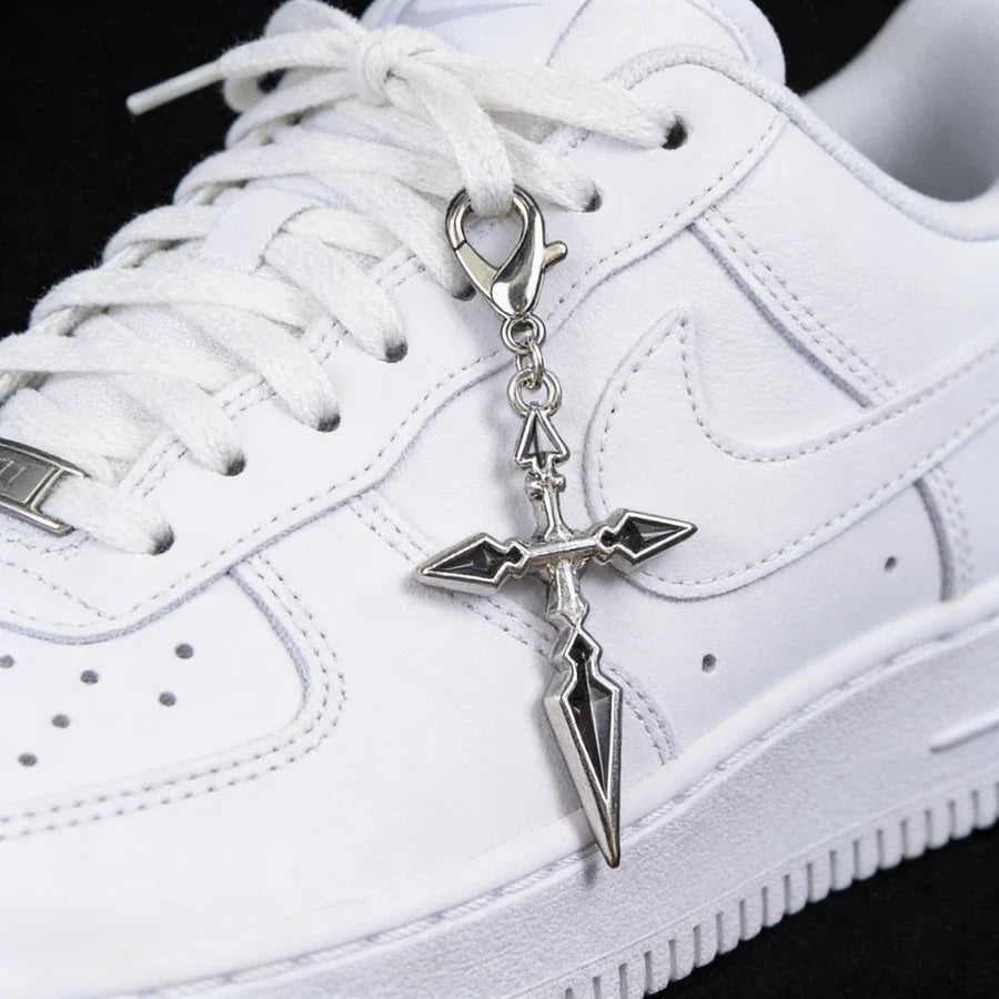 White sneaker with a silver cross-shaped keychain on a black background