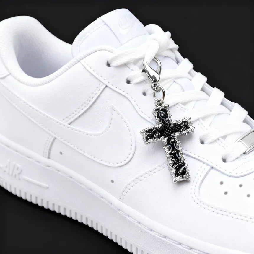 White sneaker with a black cross charm on a black background