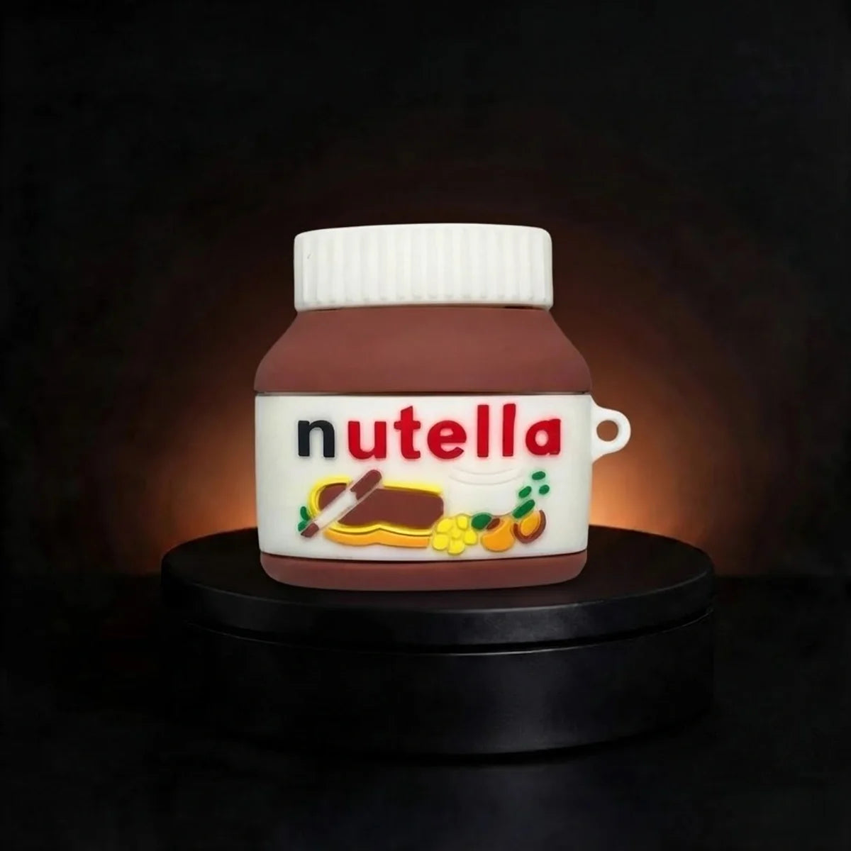 A small sculpted airpods case shaped like a Nutella jar, with a white cap, brown body, and a front label reading 'nutella' in red letters, displayed on a black pedestal against a dark background.