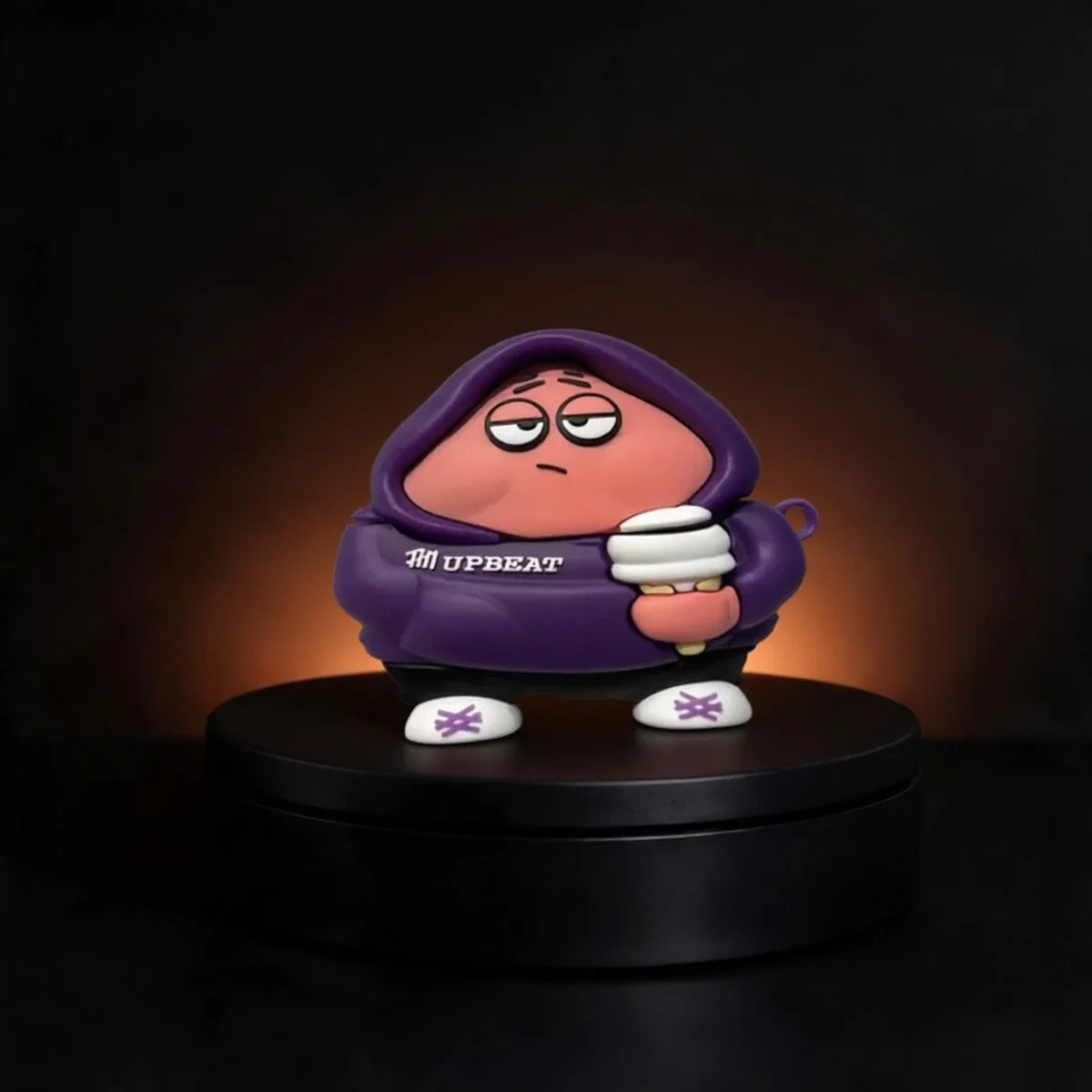 A stylized collectible figure of a pink character Patrick from spongebob case for airpods and buds wearing a purple hoodie with 'UPBEAT' printed on the chest, standing on a black circular platform against a dark background with warm light glow.