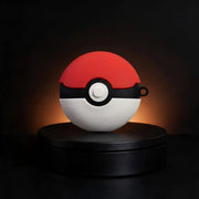 A red and white spherical device with a black horizontal band and central white button, styled like a Pokéball, displayed on a black circular pedestal against a dark background with warm light glow.
