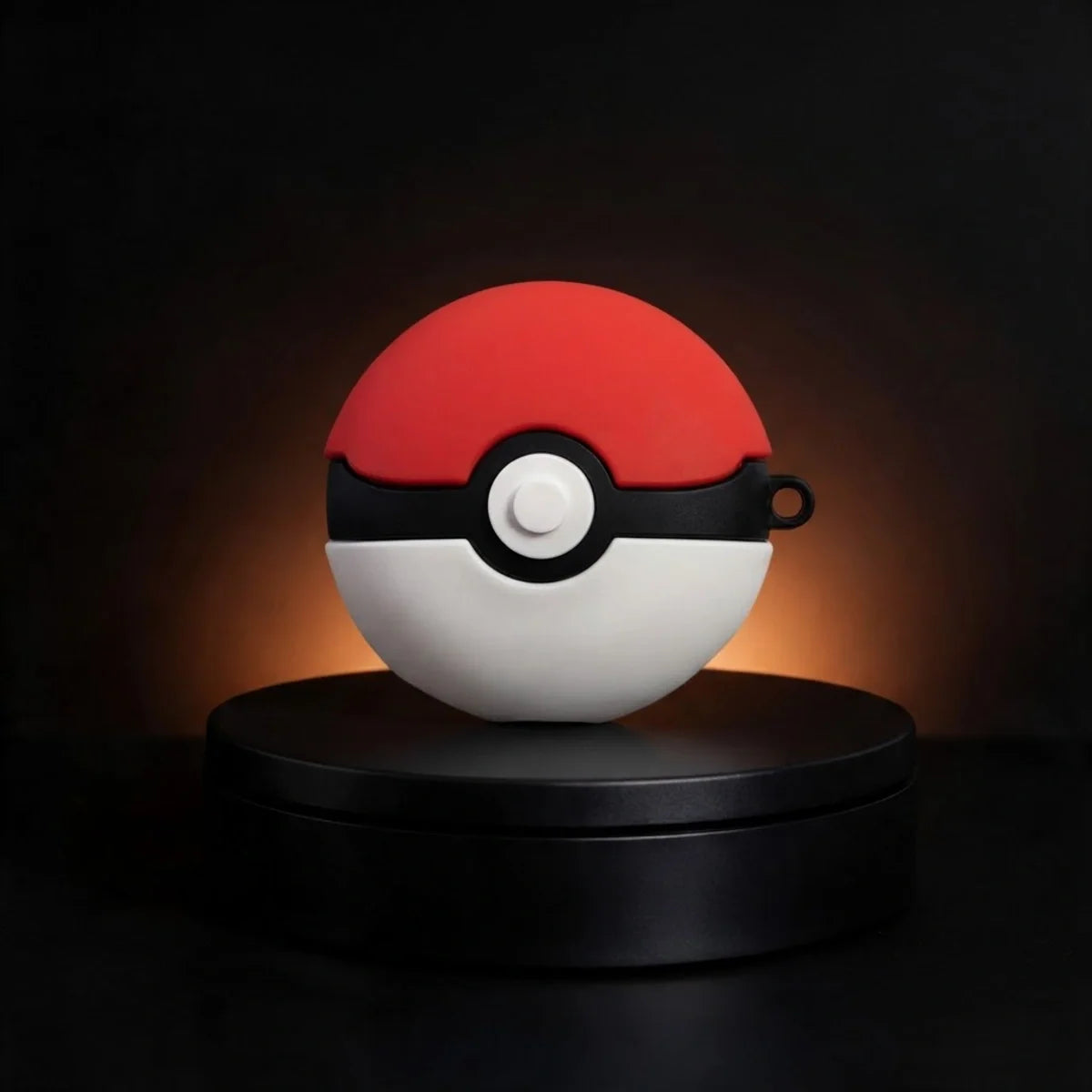 A red and white spherical device with a black horizontal band and central white button, styled like a Pokéball, displayed on a black circular pedestal against a dark background with warm light glow.